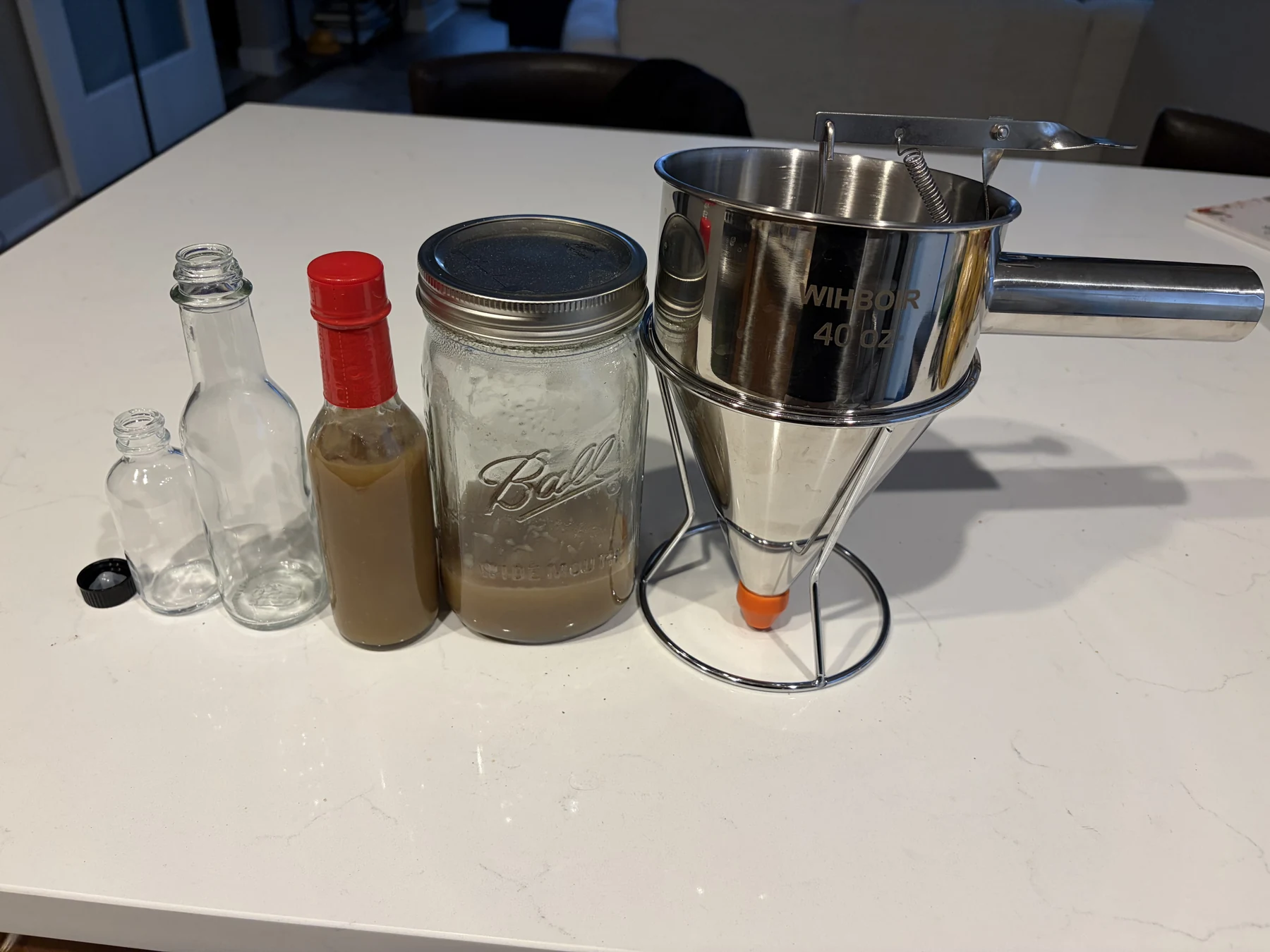 A simple bottling setup with bottles, a mason jar, and a batter dispenser ready to go.