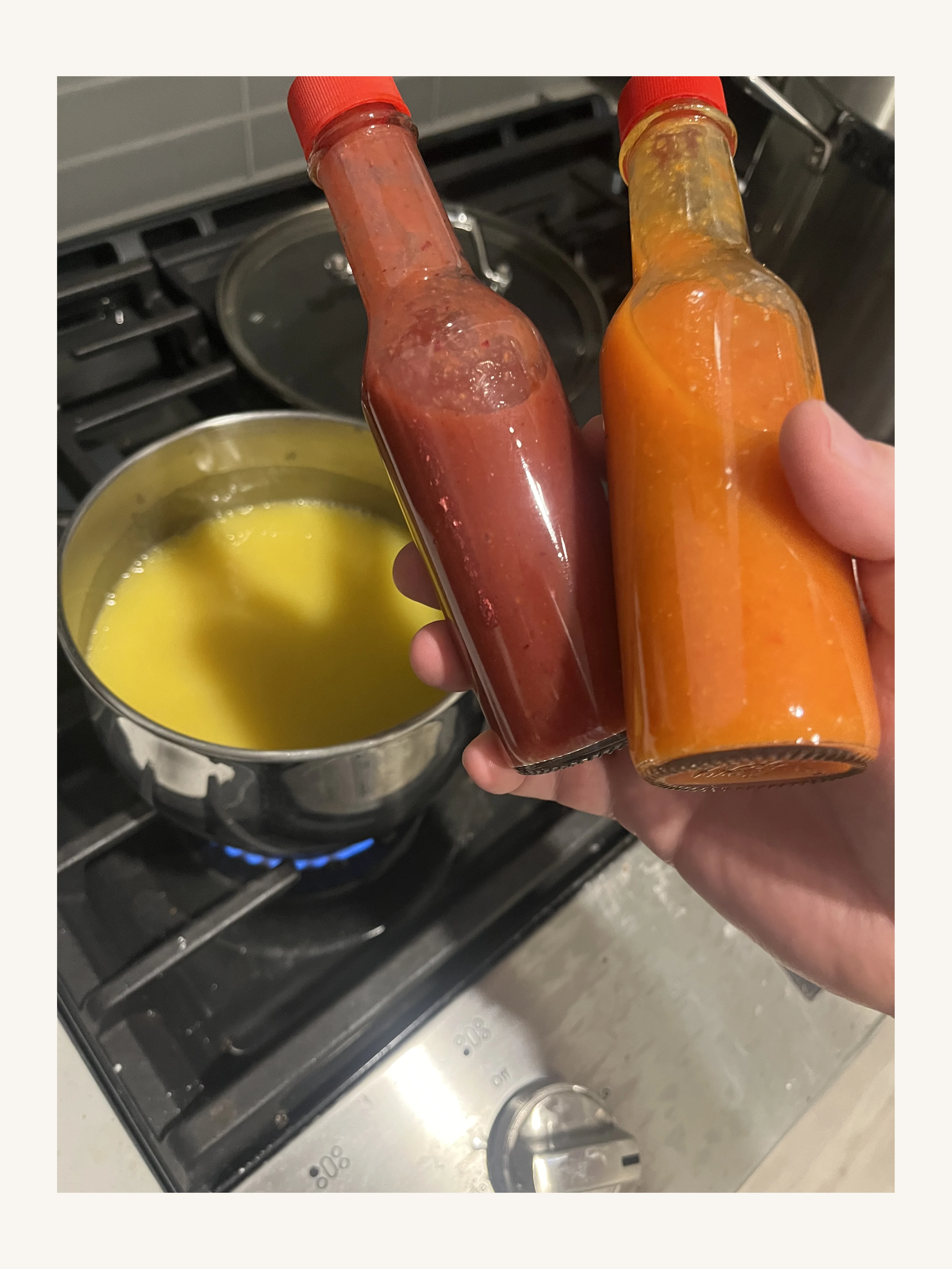Two bottles of homemade hot sauce held above a saucepan of hot sauce on the stove